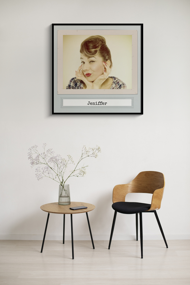 Vintage fotoposter met portret en naam in een zwarte lijst boven een bijzettafel naast een houten stoel