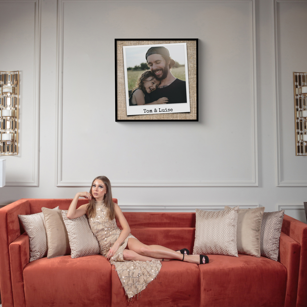 Poster de famille façon photo instantanée avec prénoms, encadré en noir sur un mur à moulures au-dessus du canapé rouge