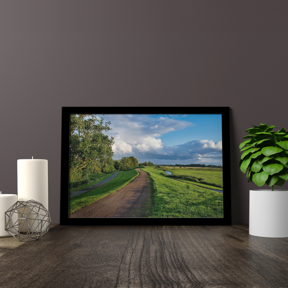 Landschapsfoto op plexiglas in een zwarte lijst op een houten blad naast kaarsen en een plant