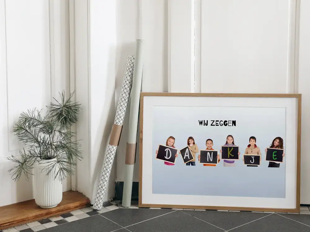 Fotocollage met kinderen en krijtbordjes met letters, in een houten lijst op de tegelvloer naast een plant