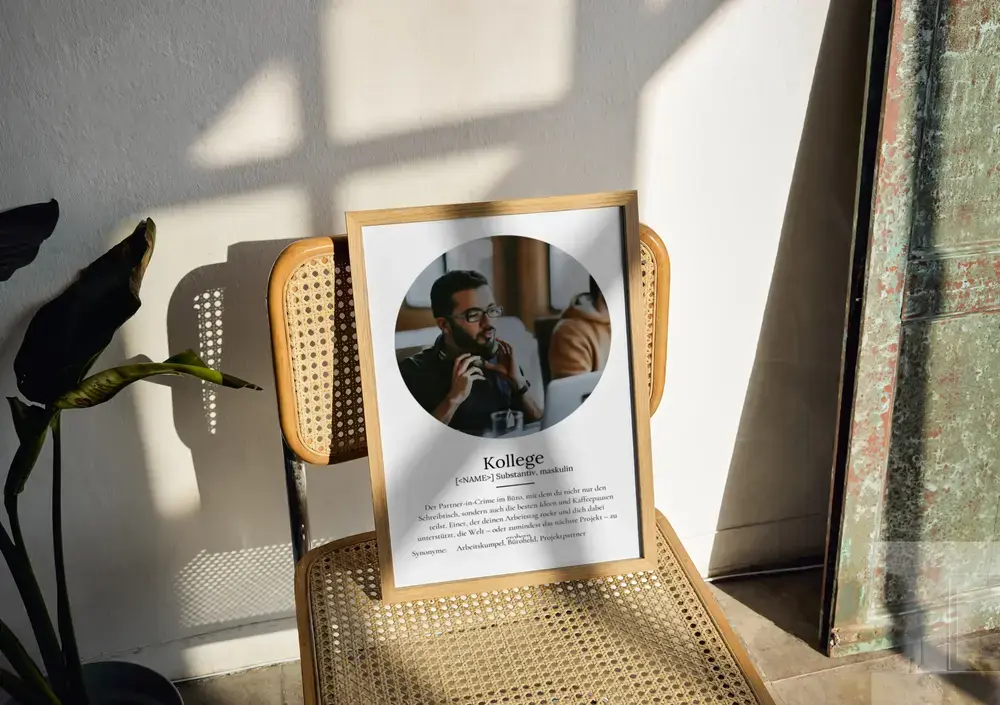 Definitionsposter für Kollegen mit ovalem Foto und Text im hellen Holzrahmen auf einem Stuhl im Sonnenlicht