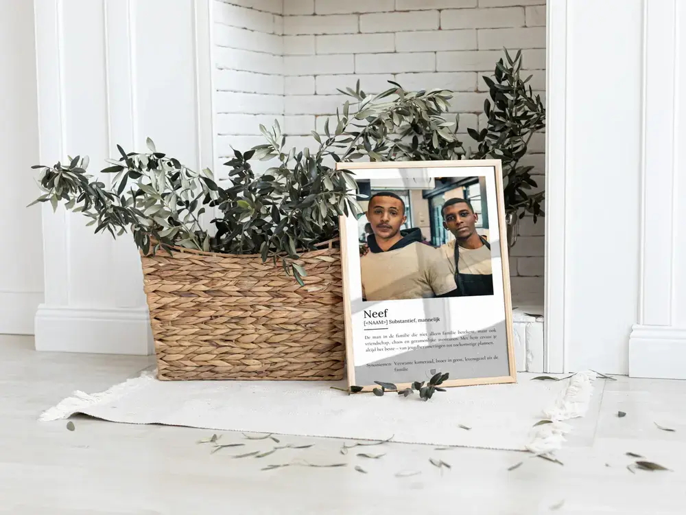 Poster voor een neef met foto en persoonlijke definitie, in een lichte lijst op de vloer naast een plantenmand