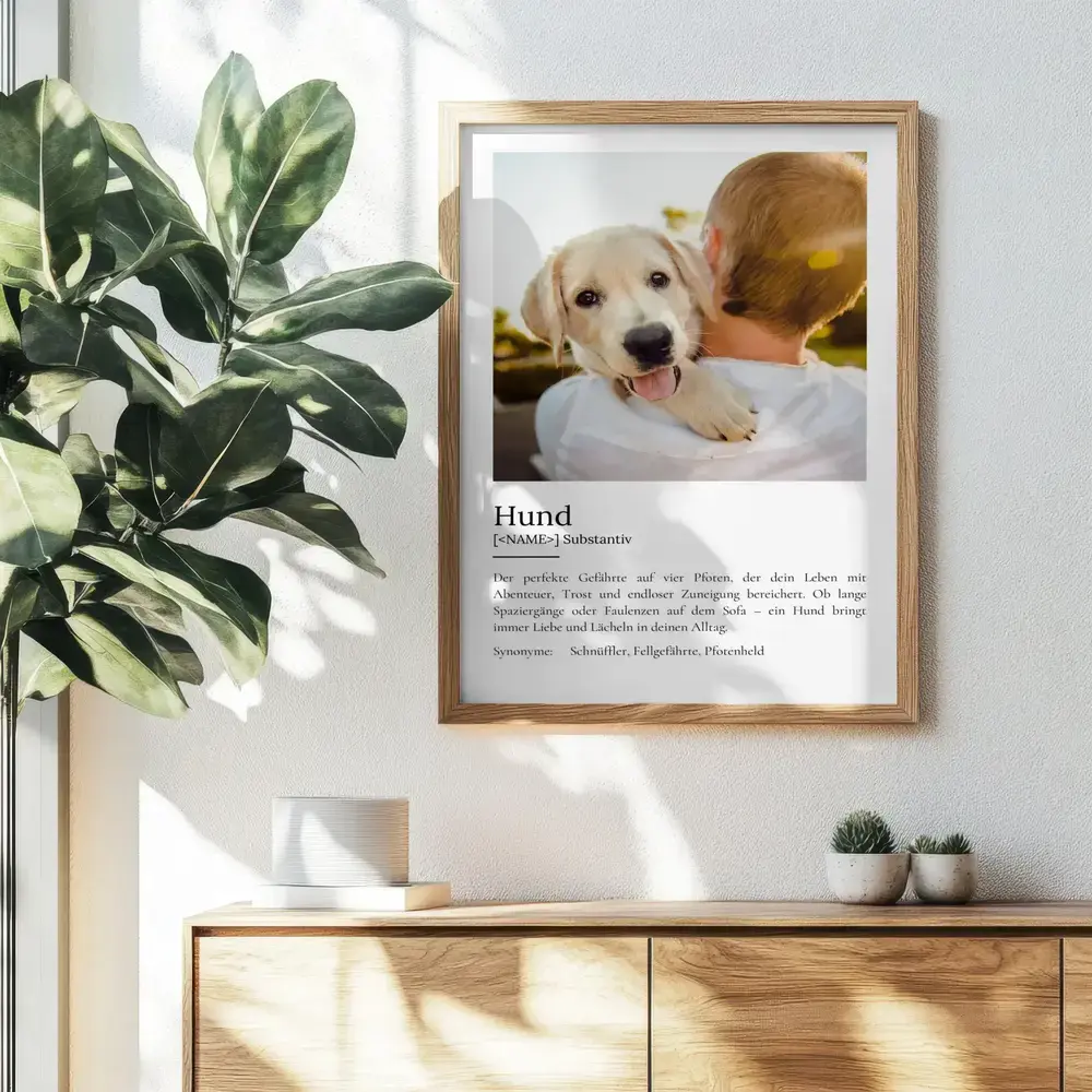 Definitionsposter mit Welpenfoto im Naturholzrahmen an der Wand über einer Holzkommode neben einer Grünpflanze
