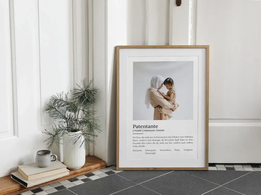 Definitionsposter für die Patentante mit Einzelfoto im Naturholzrahmen, am Boden neben Büchern und Pflanze