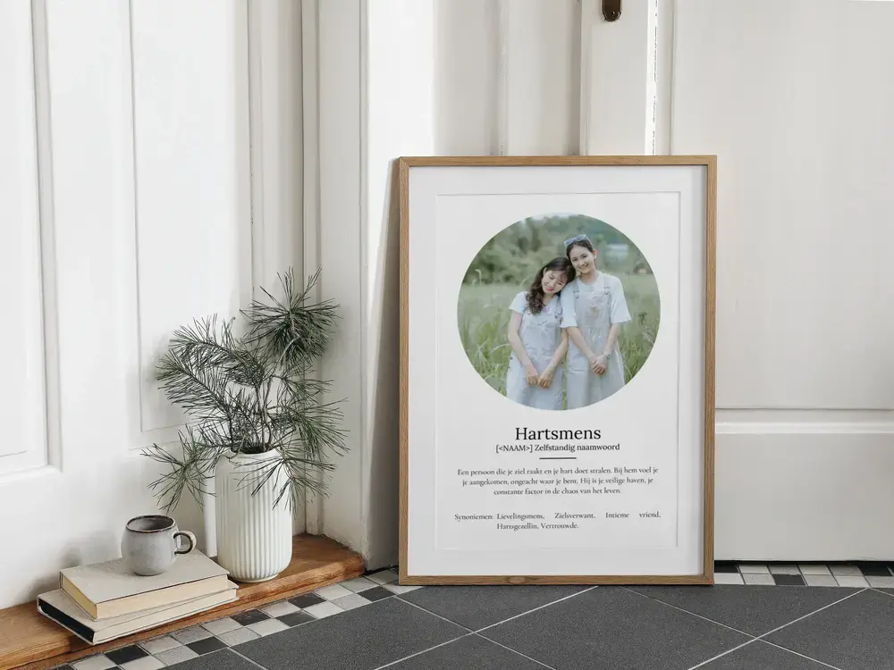 Definitieposter met ronde vriendinnenfoto in houten lijst, op de vloer naast een plant en boeken