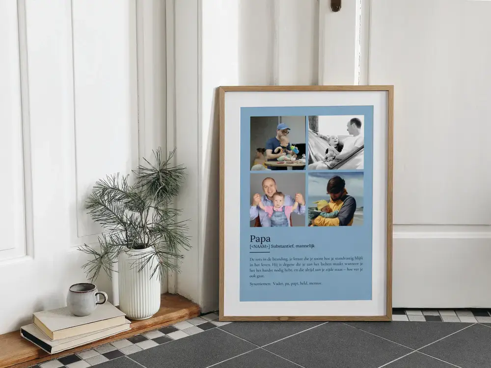 Blauwe poster met vier foto's en een definitie van papa, in een houten lijst op de tegelvloer naast een vaas