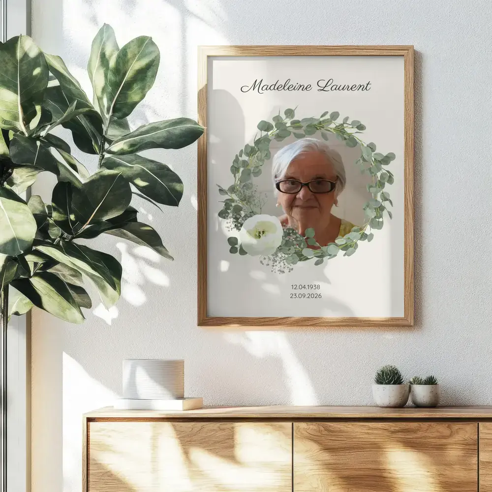 Portrait commémoratif avec couronne d’eucalyptus et fleurs blanches, encadré en bois au mur au-dessus d’un buffet