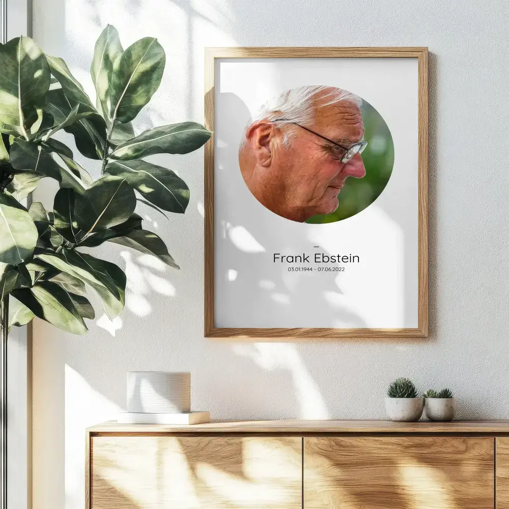 Herdenkingsfoto met rond portret en naam in een naturel houten lijst boven een dressoir naast een plant