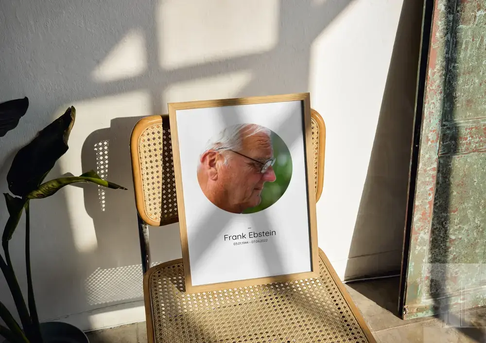 Herdenkingsfoto met rond portret, naam en levensdata in een houten lijst op een stoel met webbing in het zonlicht