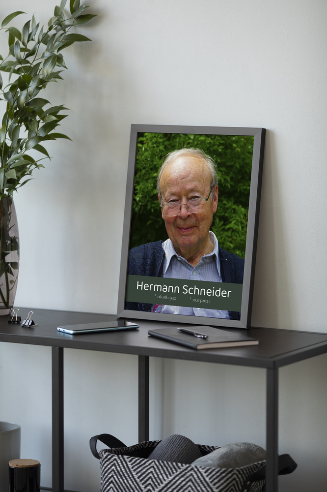 Gerahmtes Gedenkfoto mit Porträt, Namen und Lebensdaten auf dunkelgrünem Banner, auf einem Schreibtisch aufgestellt